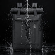 Le Nomade, sac à dos ordinateur Roll Top noir sous un jet d’eau